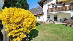 A two-story building with a balcony, a well-maintained lawn, and a mountain in the background. - Apartment 'Typ A Pöder's Haus' with Mountain View, Shared Garden and Wi-Fi (Naturno)