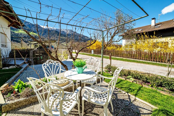Une terrasse avec des chaises et une table en métal blanc, entourée d’un jardin planté et offrant une vue sur une montagne.