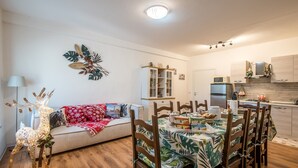 A cozy living room with a sofa, a dining table with chairs, a decorative reindeer, and a kitchen area with cabinets and appliances.