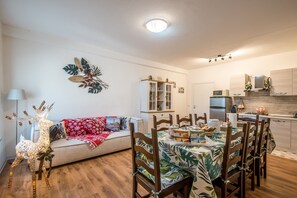 A cozy living room with a sofa, a dining table with chairs, a decorative reindeer, and a kitchen area with cabinets and appliances.