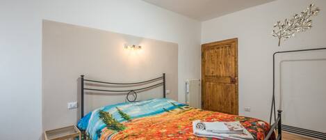 A bedroom with a bed, a wooden door, a radiator, and a wall-mounted light fixture.