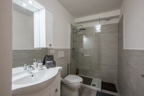 A modern bathroom with a glass-enclosed shower, a white sink, and a toilet.