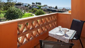Un balcon avec une table et des chaises, donnant sur un paysage côtier avec des maisons et de la végétation.
