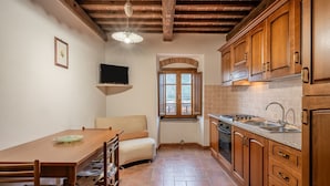 Cocina compacta con armarios de madera, una mesa de comedor, un sofá y un televisor montado en la pared.