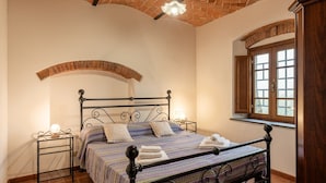 Una habitación con una cama, una ventana, techo de ladrillo y puerta de madera.