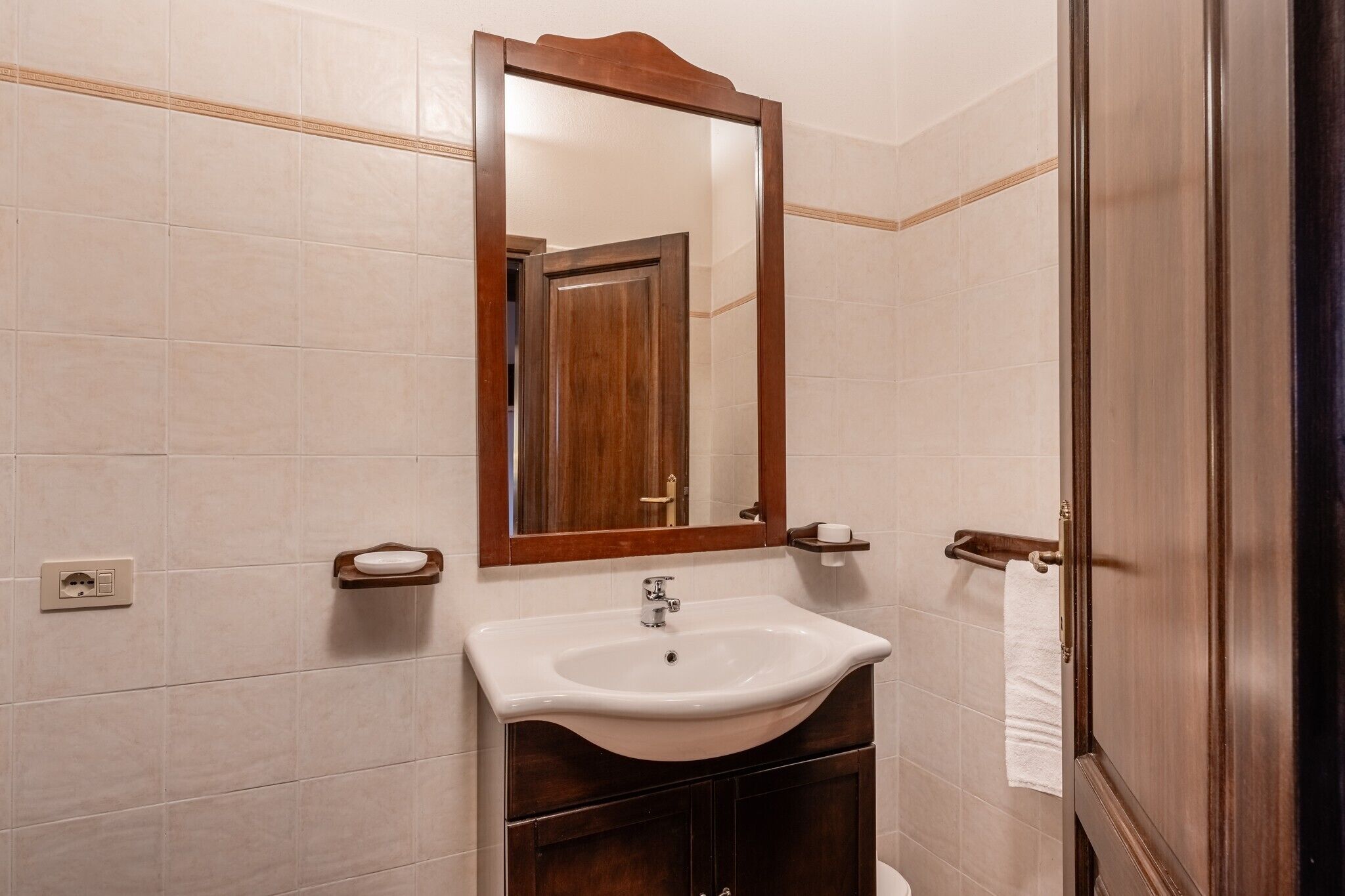 Une salle de bain avec un lavabo blanc, un miroir encadré en bois et un porte-serviettes.