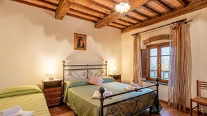Een slaapkamer met een bed, nachtkastjes, een stoel, een raam met gordijnen en een houten plafond.