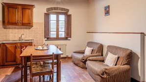 Een keuken met houten kastjes, een eettafel met stoelen, een radiator en een raam met uitzicht.