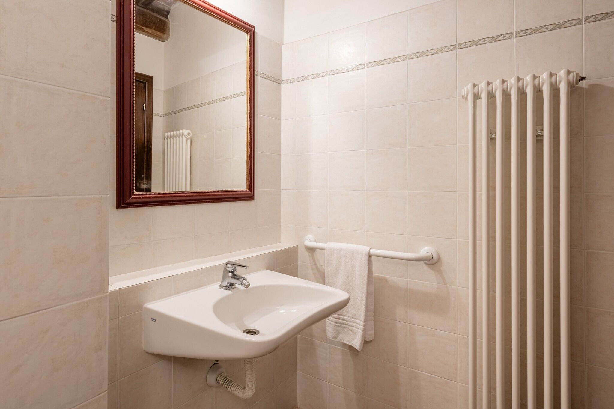 A bathroom with a sink, mirror, towel rack, and radiator.