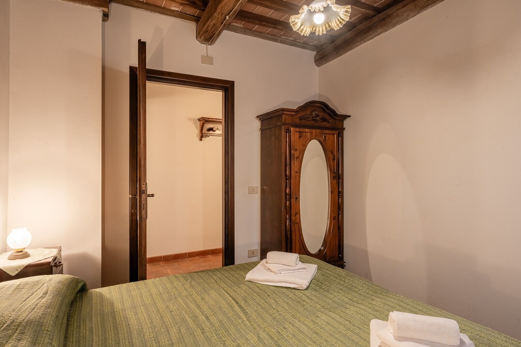 Een slaapkamer met een bed, een houten garderobe met spiegel, een deur en een nachtkastje met lamp.