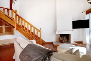 A living room with a wooden staircase, a fireplace, a flat-screen TV, and a sofa. - Apartment 'A Casa Da Concha' with Sea View, Balcony and Wi-Fi (M.nha Grande)