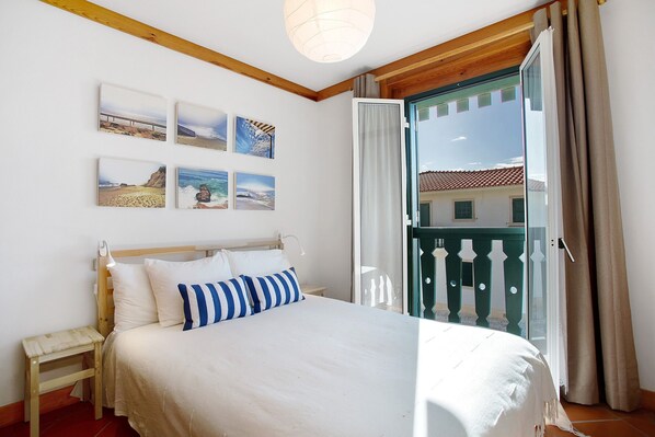 A bedroom with a bed, a nightstand, a window with curtains, and wall art.