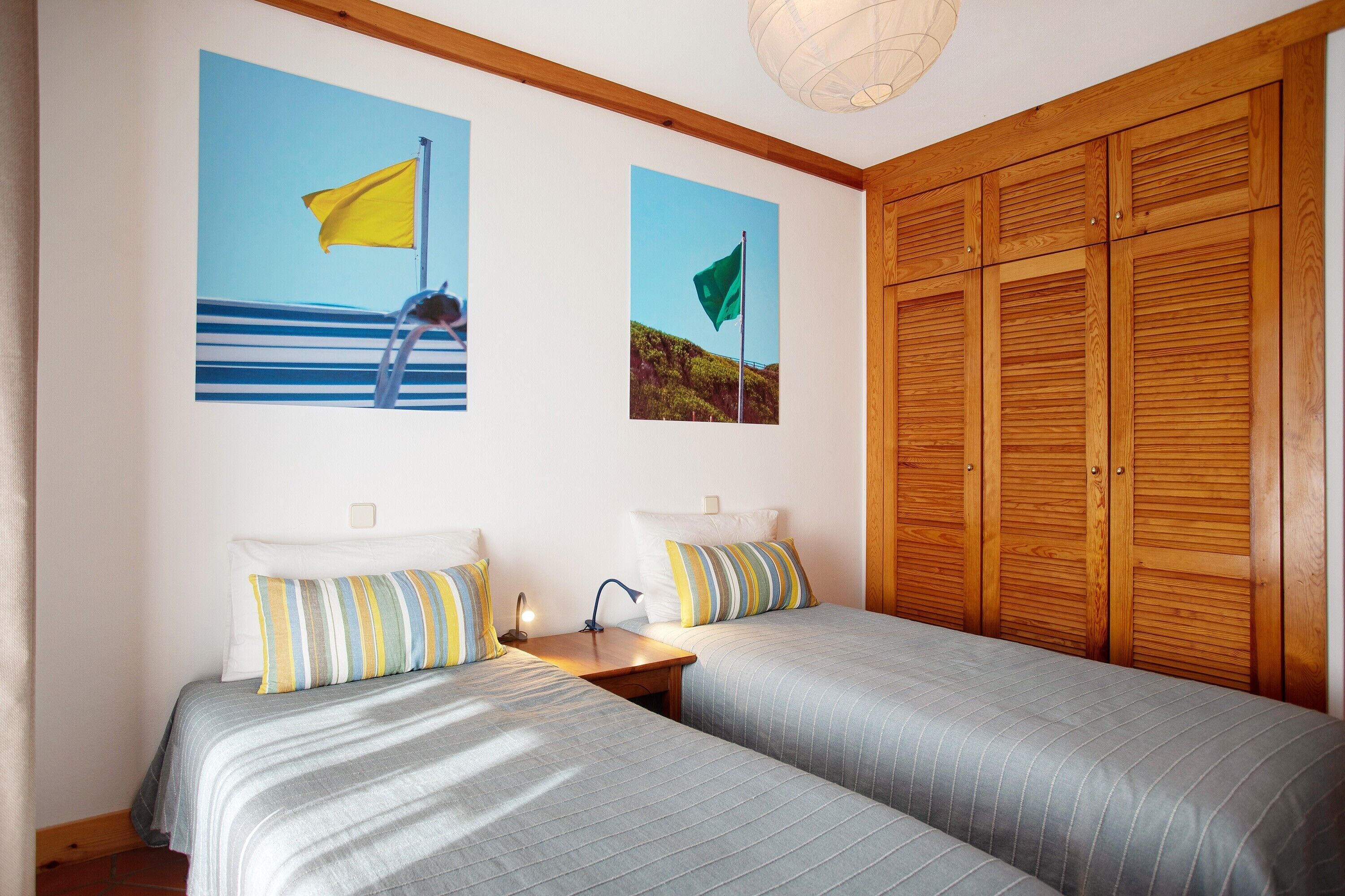 A bedroom with two beds, wooden wardrobe, and two wall-mounted pictures.