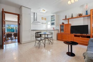 A modern kitchen with white cabinets, a dining area with chairs, a TV, and a small table.