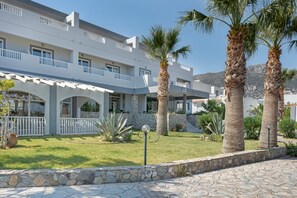 A modern building with balconies, palm trees, and a stone pathway. - Studio Apartment 'Evripides Triple Room 1' with Shared Pool, Shared Garden and Air Conditioning (Kardamaina)