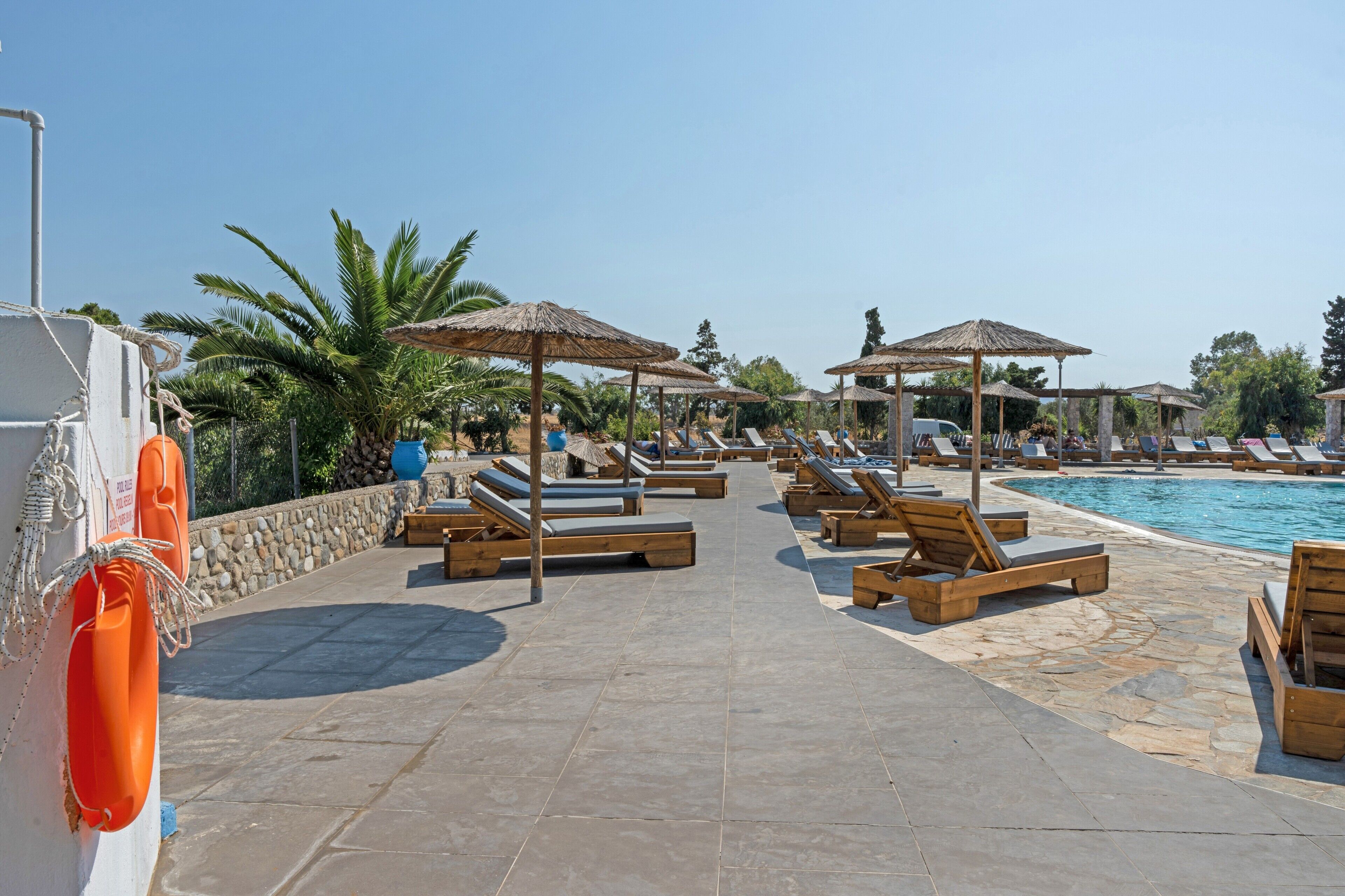 A poolside area with lounge chairs and umbrellas, a lifebuoy, and a stone wall.