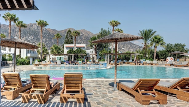 A pool area with wooden loungers, umbrellas, and a mountain backdrop. - Studio Apartment 'Evripides Triple Room 2' with Shared Pool, Shared Garden and Air Conditioning (Kardamaina)