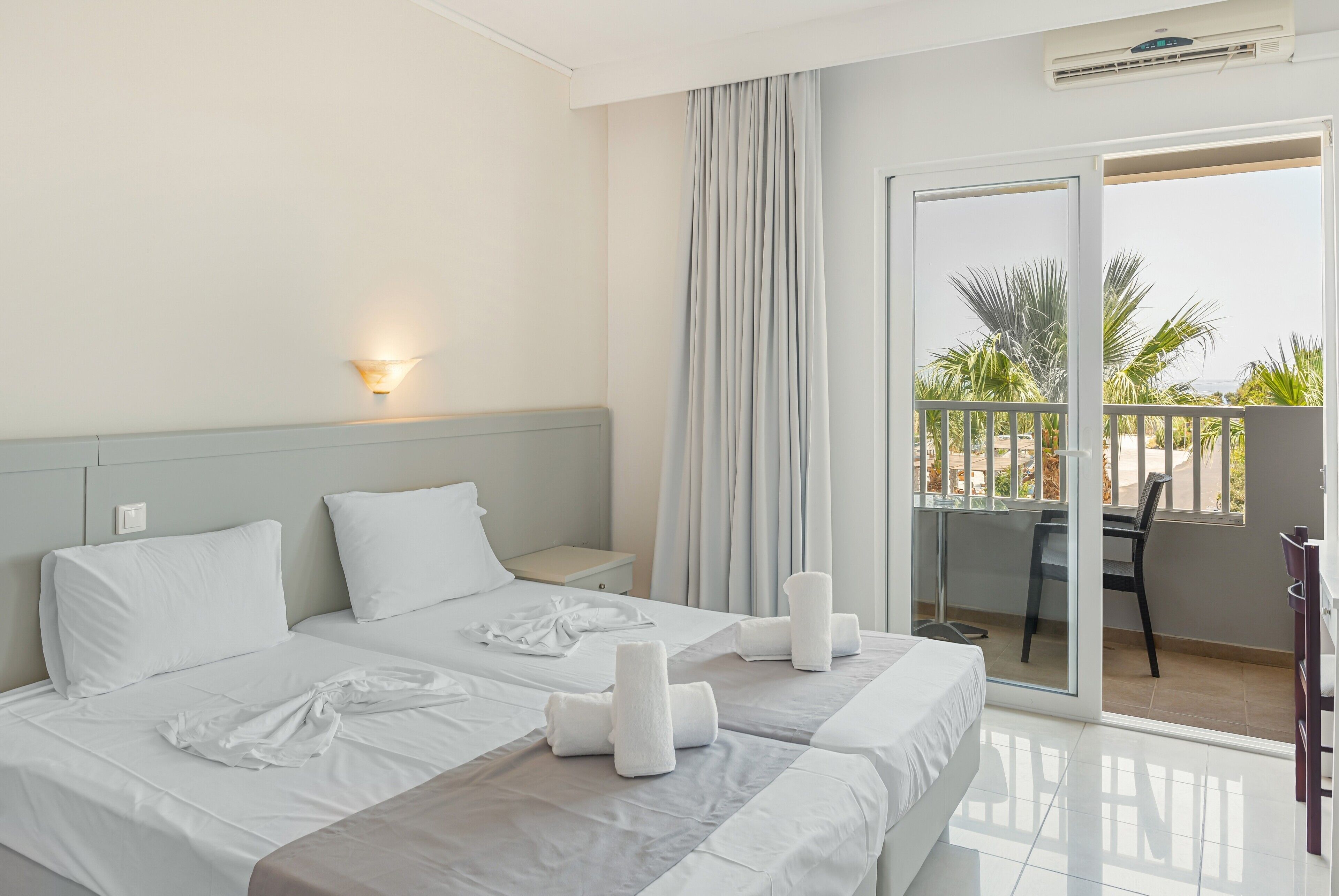 A hotel room with two beds, a balcony with a view, a desk, and a chair.