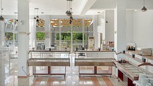 Un restaurante moderno con un interior limpio y blanco, vitrinas de cristal y una zona de estar central con vistas a zonas verdes exteriores.