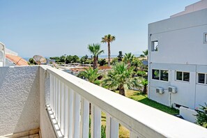Un balcon doté d’une balustrade blanche, qui donne sur un quartier résidentiel avec des palmiers et un immeuble équipé de climatiseurs.