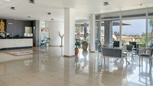 Un vestíbulo amplio con mostrador de recepción, zona de estar y grandes ventanales con vistas al exterior.