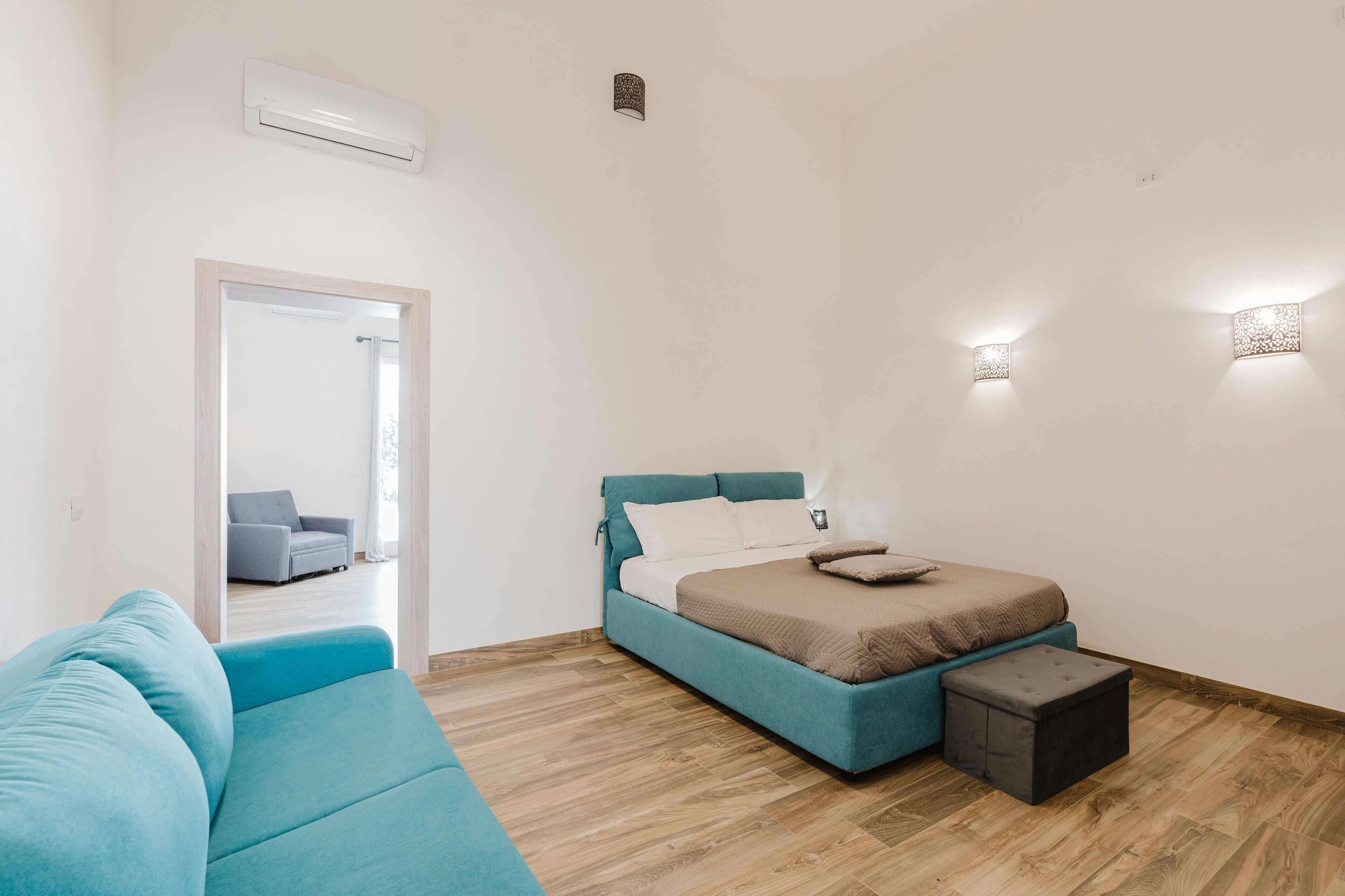 Une chambre à coucher avec un lit, un canapé bleu, un petit pouf et un miroir.