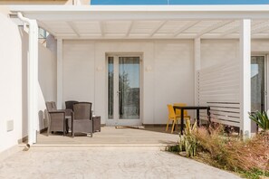 A covered outdoor patio with wicker furniture, a glass door entrance, and a small garden area.