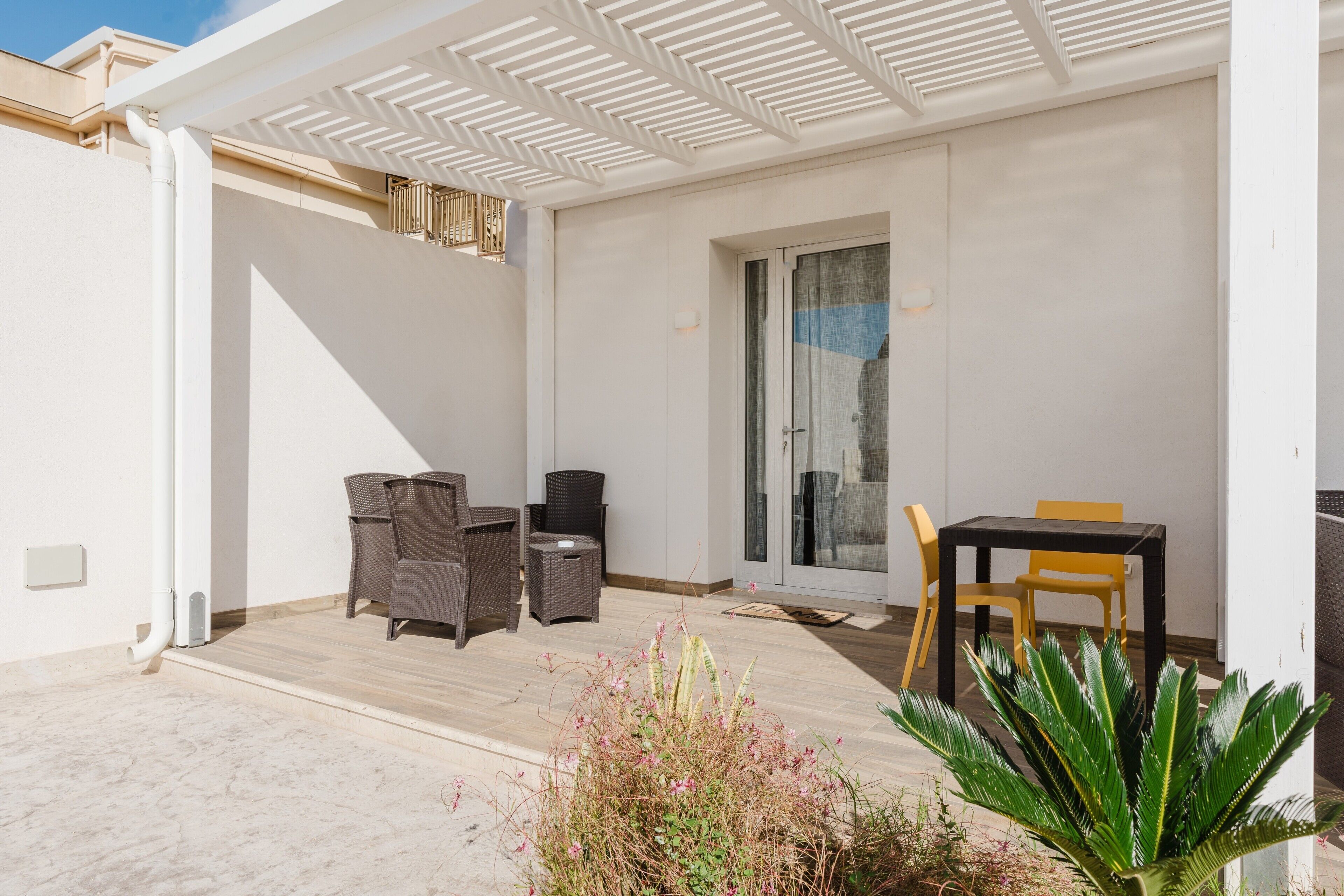 Un patio cubierto con muebles de mimbre, una puerta corrediza de vidrio y una planta en maceta.