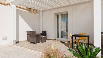 Un patio cubierto con muebles de mimbre, una puerta corrediza de vidrio y una planta en maceta.
