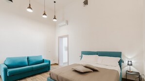 Une chambre à coucher avec un lit, un canapé bleu, une table de chevet avec une lampe et un luminaire suspendu.