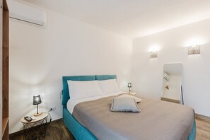 A bedroom with a bed, bedside tables, a lamp, an air conditioner, and a mirror.