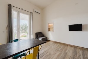Um quarto com uma mesa de jantar, cadeiras, um sofá, uma TV fixada na parede e um aparelho de ar condicionado.