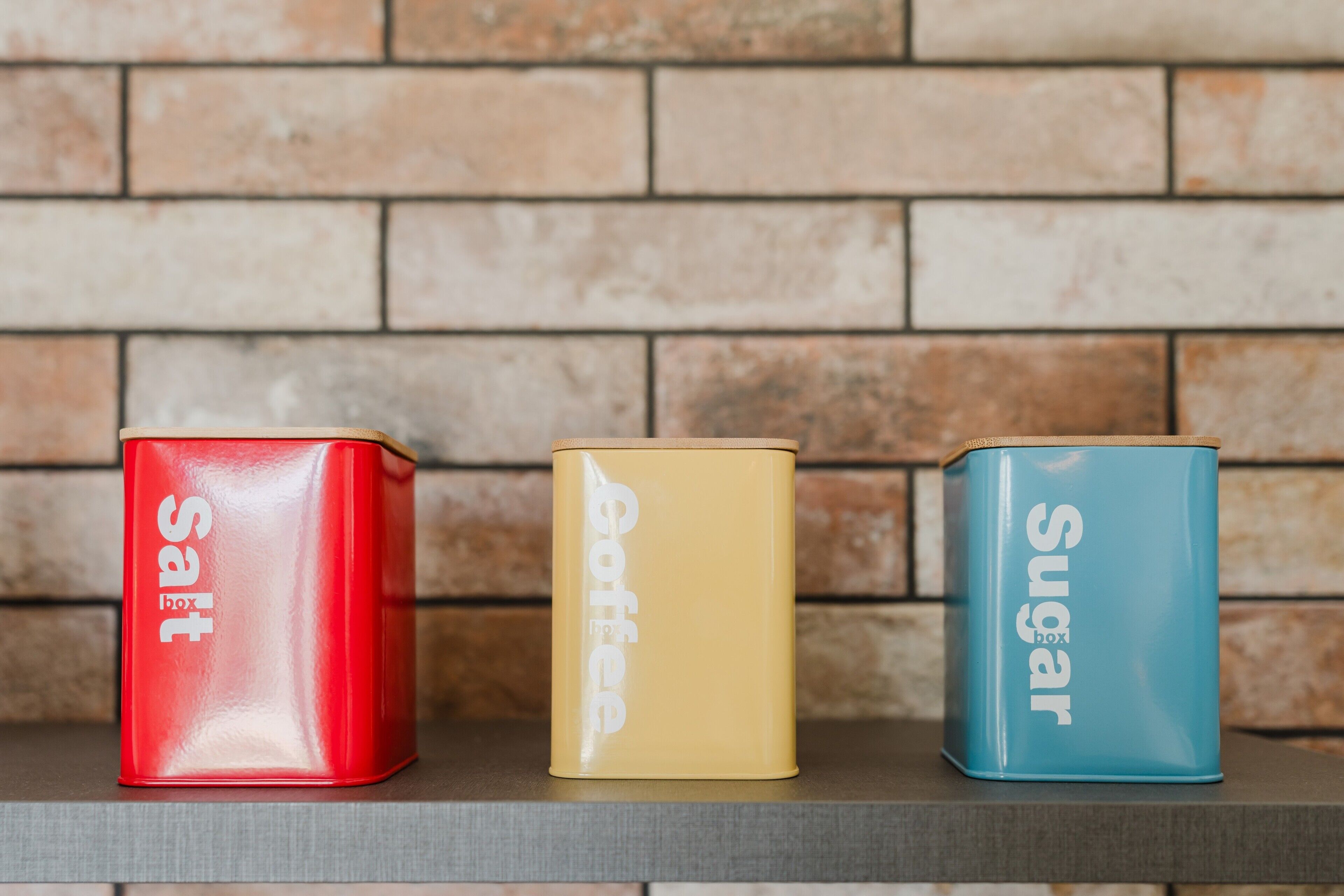 Three containers labeled 'salt,' 'coffee,' and 'sugar' on a shelf against a brick wall.