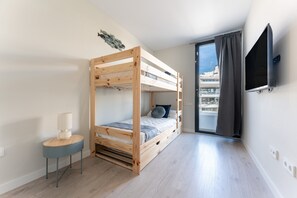 Un lit superposé avec une petite table à côté, un téléviseur fixé au mur et une vue sur la ville par la fenêtre.
