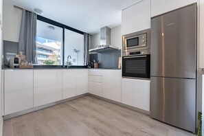Une cuisine moderne avec des meubles blancs, un réfrigérateur Bosch, un four à micro-ondes et une fenêtre avec des rideaux.