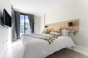 Una camera da letto moderna con un ampio letto, una TV a parete e una finestra con tende.