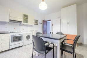 Une cuisine compacte équipée d’une cuisinière, d’un four et d’un lave-linge, d’une table à manger avec des chaises et de placards blancs.