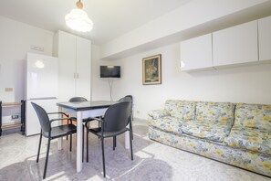 A modern kitchen with a refrigerator, a dining table with chairs, a flat-screen TV, and a floral sofa.
