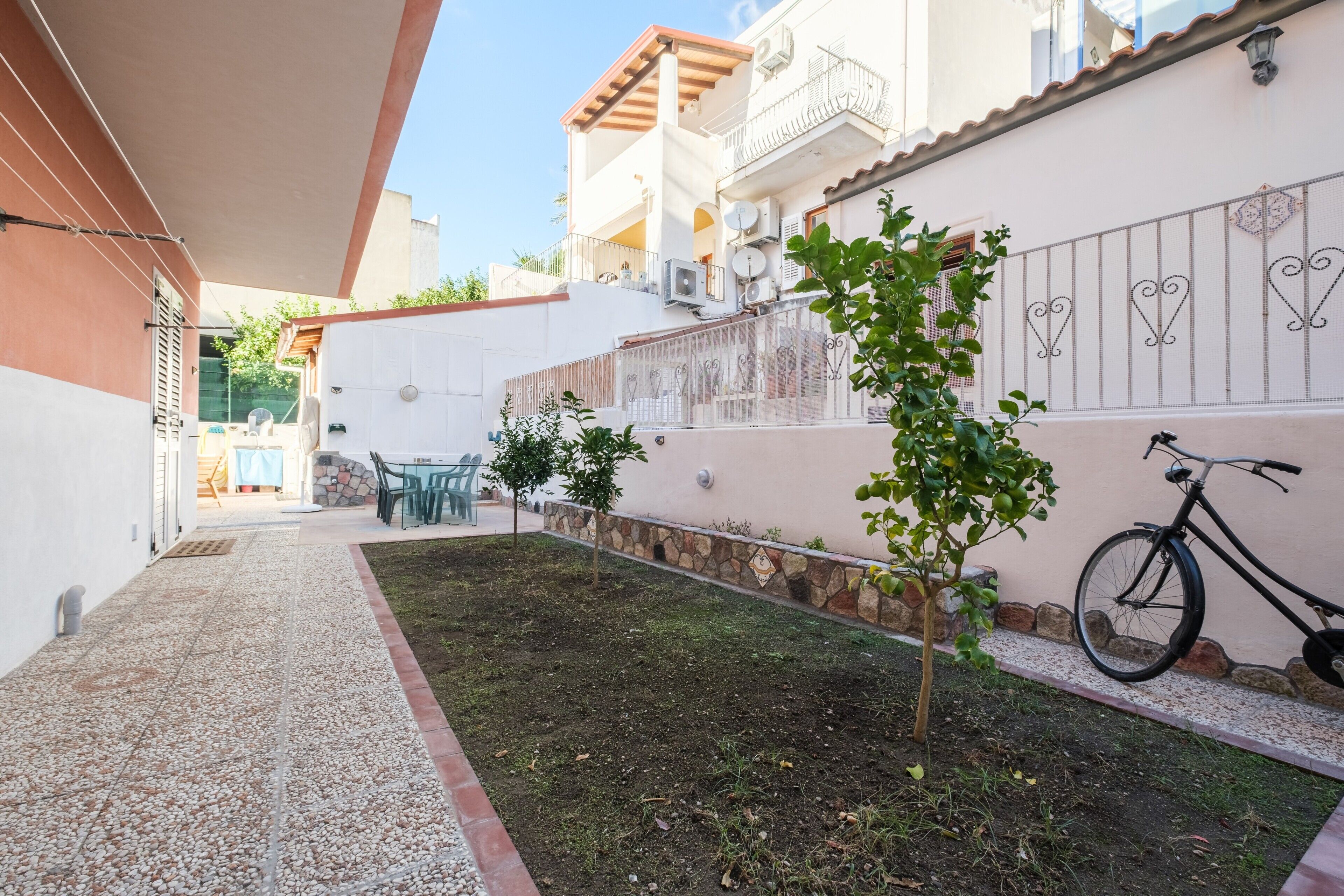A narrow pathway leading to a building with a balcony, a bicycle, and a small tree.