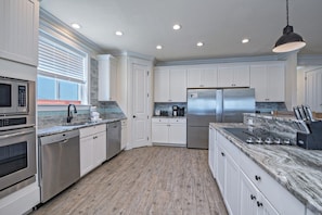 A modern kitchen with white cabinets, stainless steel appliances, and a marble countertop.