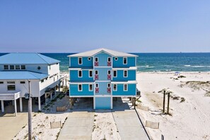 A multi-story building with a blue facade and white roof, located on a sandy beach with the ocean in the background. - BeachFront 9Bed EasyBreezy West (Gulf Shores)