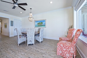 A dining area with wicker chairs and a table, a ceiling fan, a chandelier, and a framed picture on the wall.