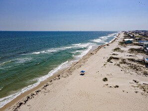 Una playa con vistas claras al océano, una orilla arenosa y algunos edificios al fondo.