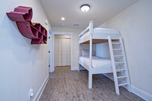 Een slaapkamer met stapelbedden, een houten vloer, witte muren en een deur op de achtergrond.