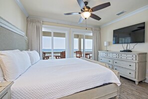 A large bed with a quilted white duvet, a ceiling fan, a television, a dresser, and a view of the ocean through large windows. - BeachFront 9Bed EasyBreezy West (Gulf Shores)