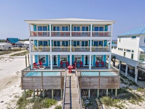 Een meerlaags gebouw aan het strand, met een zwembad, terras en een houten dek.