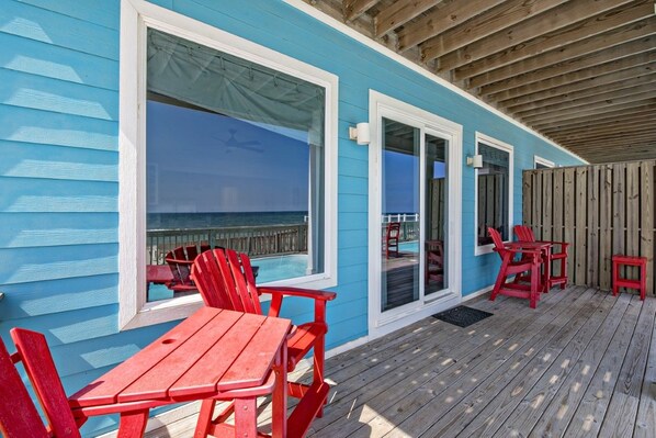 A blue building with large windows overlooking the ocean, a wooden deck with red chairs and tables, and a wooden fence. - BeachFront 9Bed EasyBreezy West (Gulf Shores)