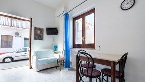 Ein Zimmer mit Esstisch, Stühlen, einer Couch, einem Fernseher und einem Fenster mit Vorhang.
