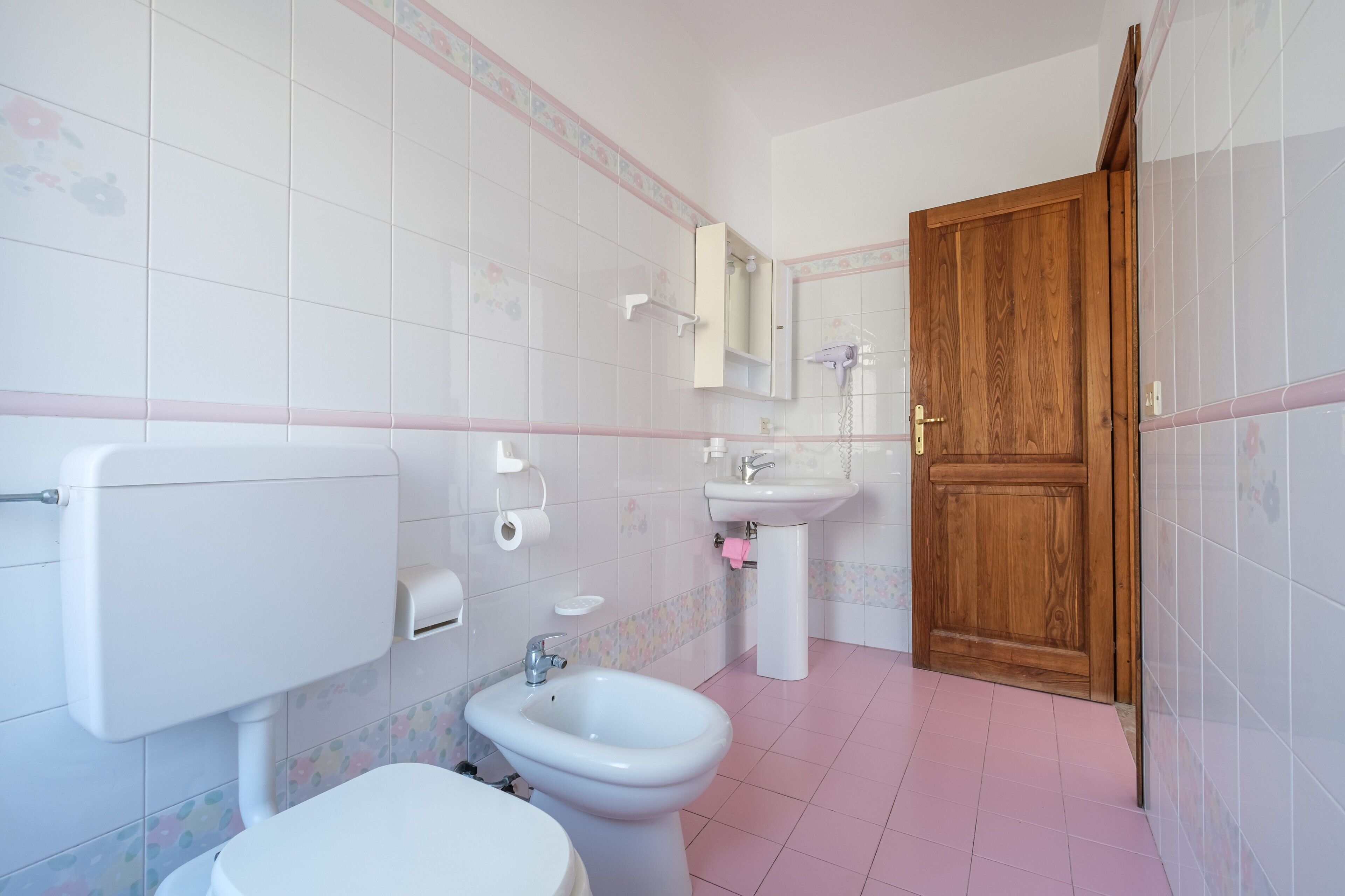 A bathroom with a toilet, bidet, sink, and wooden door.