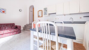 Una cocina con gabinetes blancos, encimera negra y un lavamanos. En la sala de estar, hay un sofá rojo.